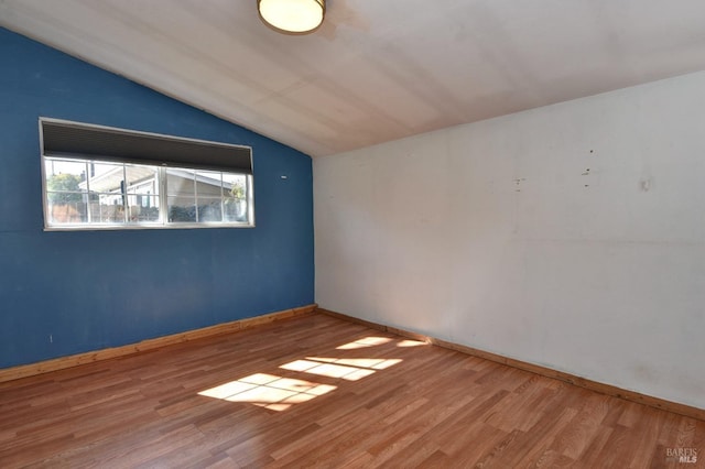 unfurnished room with lofted ceiling, baseboards, and wood finished floors