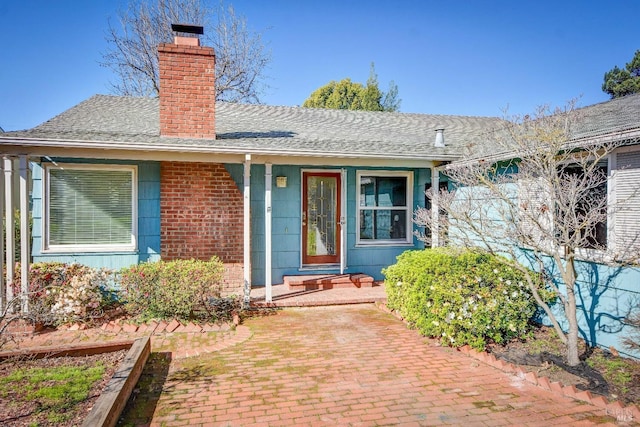 view of exterior entry featuring a shingled roof, a chimney, and brick siding