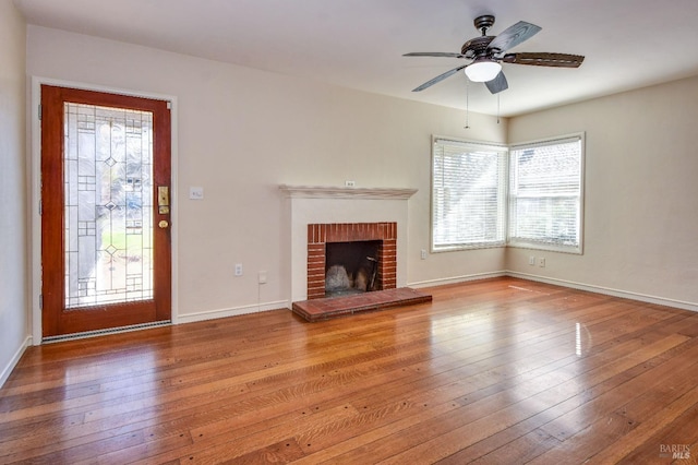 unfurnished living room featuring a brick fireplace, baseboards, ceiling fan, and hardwood / wood-style floors