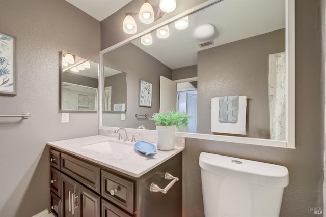 bathroom with toilet, a textured wall, visible vents, and vanity