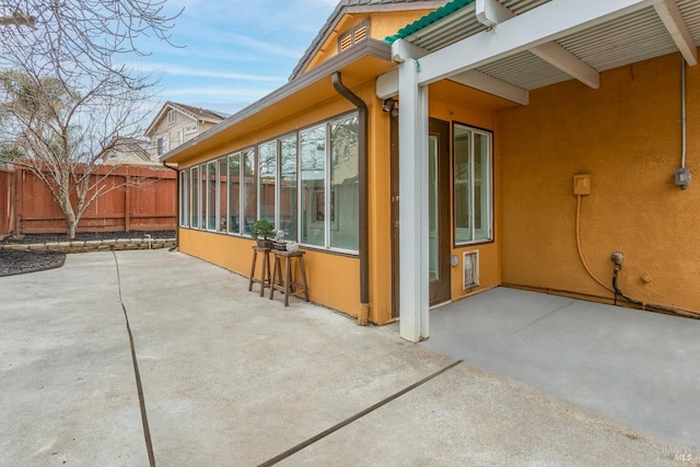 view of side of home with stucco siding, fence, and a patio