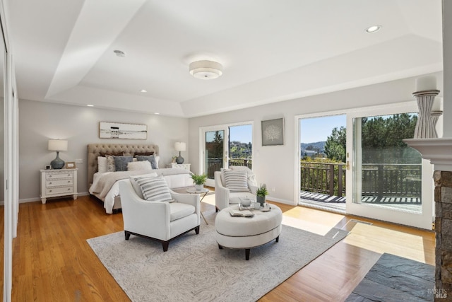 bedroom with baseboards, a raised ceiling, access to outside, light wood-type flooring, and a fireplace