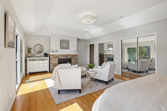 bedroom with light wood-style floors, a tray ceiling, a stone fireplace, and baseboards