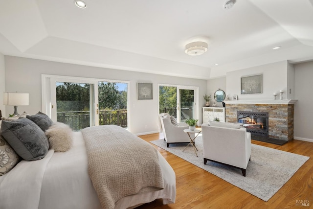 bedroom with baseboards, a glass covered fireplace, light wood-style flooring, a tray ceiling, and recessed lighting