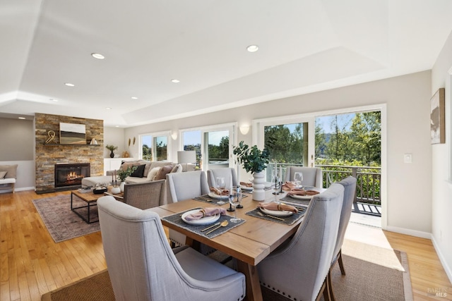 dining space with light wood finished floors, baseboards, a raised ceiling, a fireplace, and recessed lighting