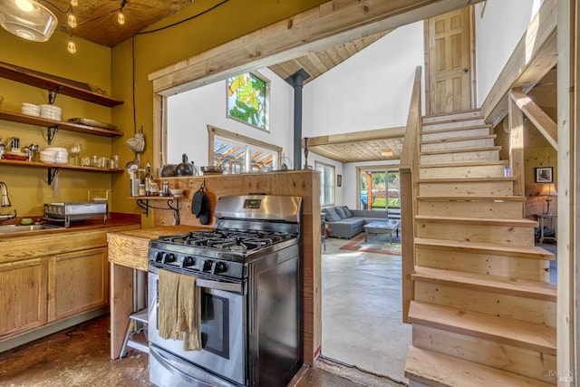 kitchen with stainless steel gas stove, vaulted ceiling, concrete floors, and a sink