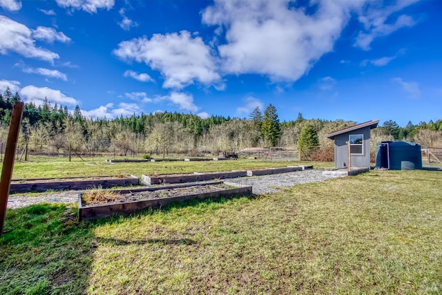 view of yard featuring an outbuilding, a vegetable garden, a view of trees, and a storage unit