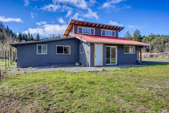 back of property featuring metal roof, a lawn, and stucco siding