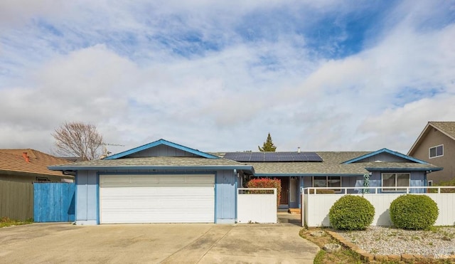 single story home featuring a garage, concrete driveway, roof with shingles, fence, and roof mounted solar panels