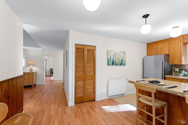 kitchen featuring brown cabinetry, freestanding refrigerator, radiator, and light countertops