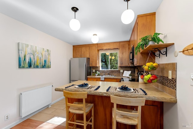 kitchen with a peninsula, light countertops, freestanding refrigerator, brown cabinets, and radiator heating unit