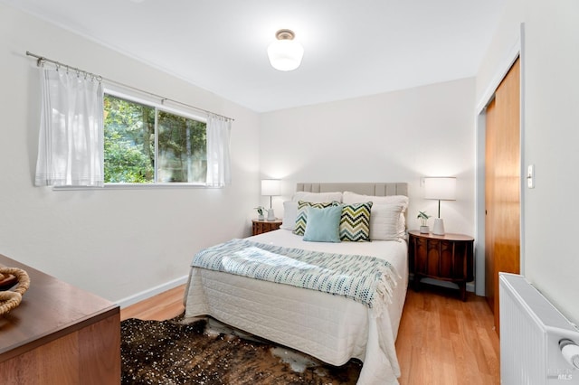 bedroom with radiator, light wood-style floors, and baseboards