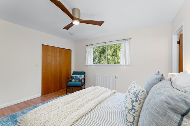 bedroom featuring wood finished floors, a ceiling fan, baseboards, a closet, and radiator heating unit