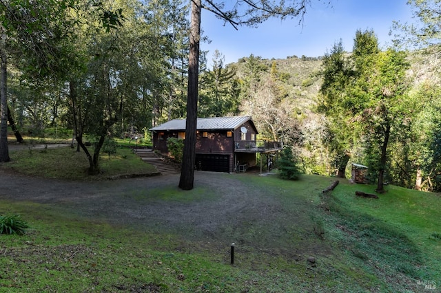 exterior space with dirt driveway, metal roof, a deck, a garage, and a front lawn