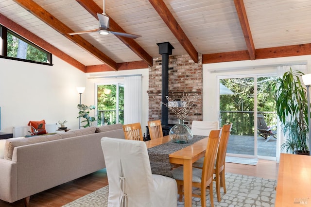 dining room featuring a ceiling fan, light wood-style flooring, wood ceiling, a wood stove, and vaulted ceiling with beams