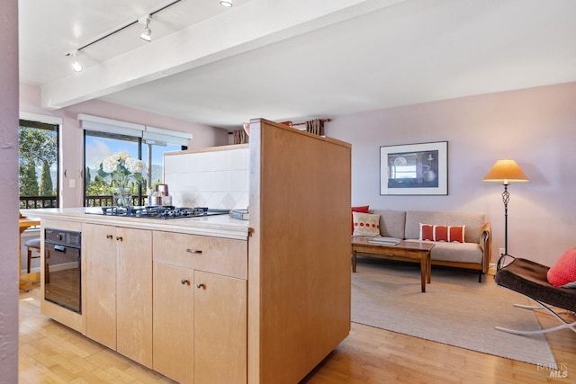 kitchen with light wood-style flooring, oven, light countertops, beam ceiling, and light brown cabinetry