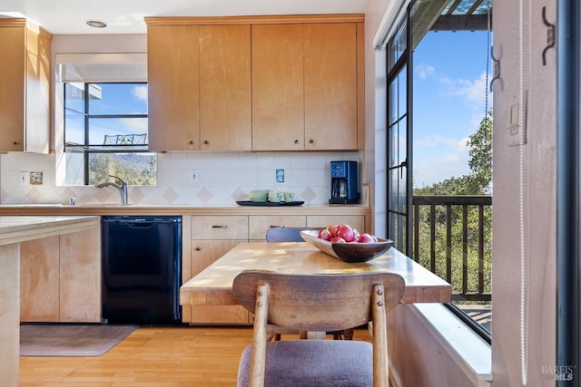 kitchen featuring a sink, black dishwasher, decorative backsplash, light wood finished floors, and breakfast area