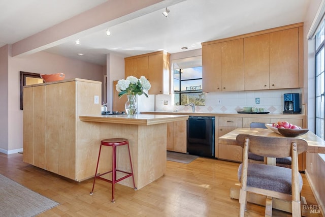 kitchen with light wood-type flooring, black dishwasher, light countertops, and beam ceiling