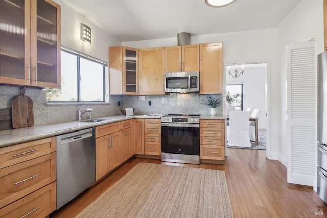 kitchen featuring decorative backsplash, appliances with stainless steel finishes, glass insert cabinets, light brown cabinets, and a sink