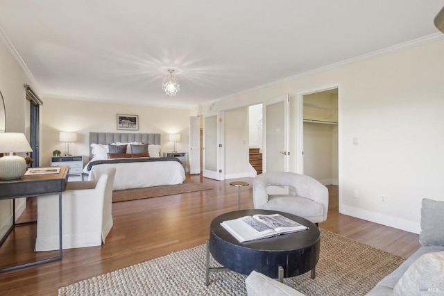 bedroom featuring ornamental molding, wood finished floors, a walk in closet, and baseboards