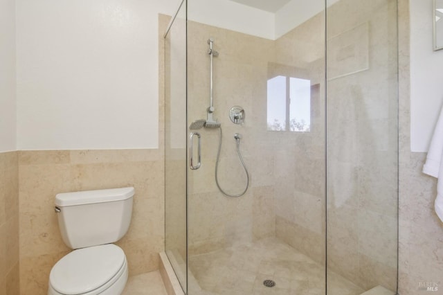 full bathroom with toilet, a stall shower, tile walls, and wainscoting