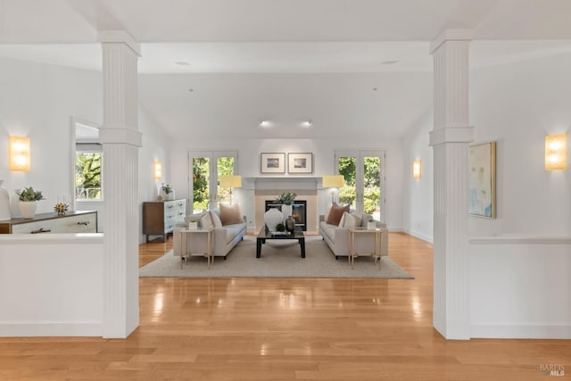 living area with lofted ceiling, ornate columns, a healthy amount of sunlight, and a glass covered fireplace