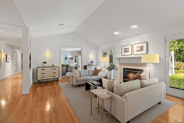 living room featuring a wealth of natural light, light wood-type flooring, a glass covered fireplace, and decorative columns