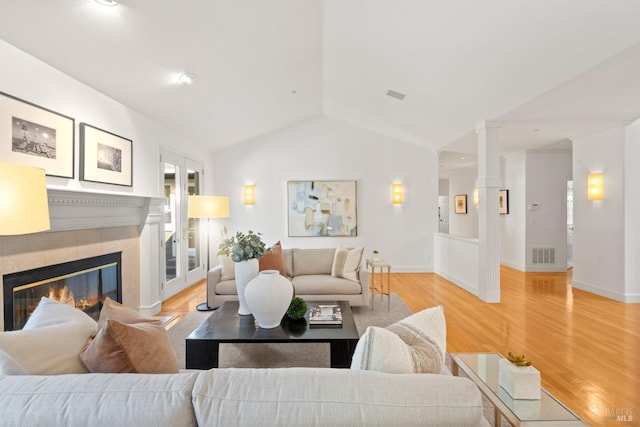 living room featuring decorative columns, visible vents, lofted ceiling, light wood-style flooring, and a fireplace