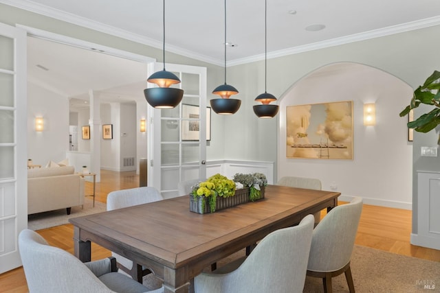 dining room with light wood finished floors, baseboards, arched walkways, and crown molding