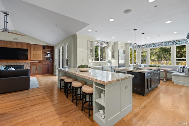 kitchen with white cabinetry, open floor plan, stainless steel built in fridge, an island with sink, and pendant lighting