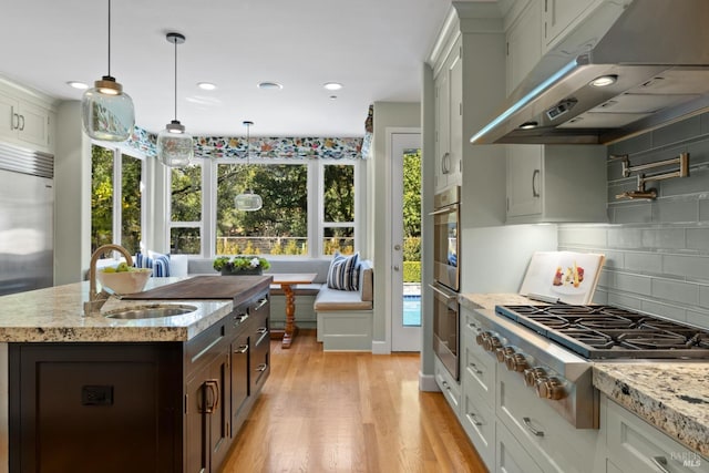 kitchen with under cabinet range hood, stainless steel appliances, a sink, white cabinets, and an island with sink