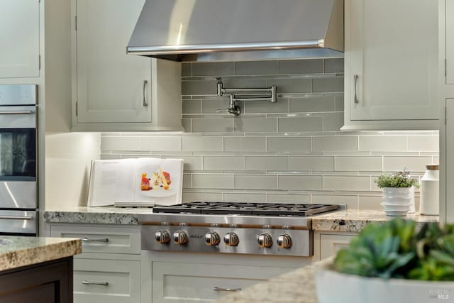 kitchen with stainless steel appliances, light stone counters, ventilation hood, and backsplash