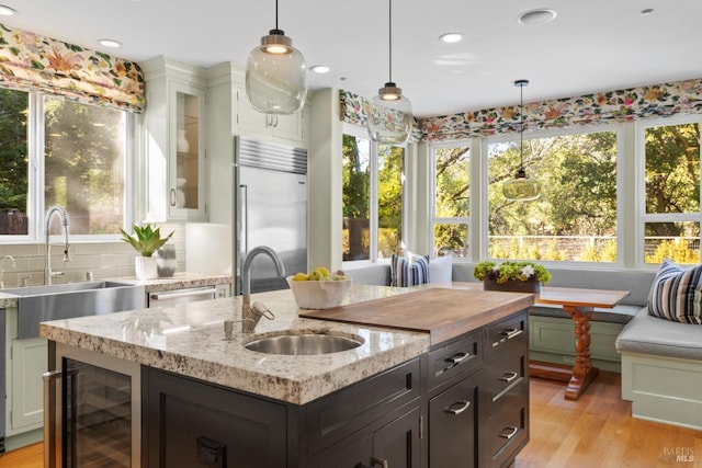 kitchen with wine cooler, breakfast area, glass insert cabinets, stainless steel built in fridge, and light stone countertops