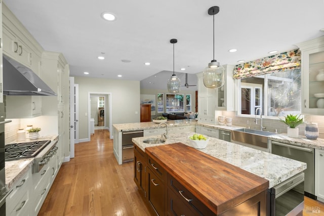 kitchen with an island with sink, light stone countertops, glass insert cabinets, and pendant lighting