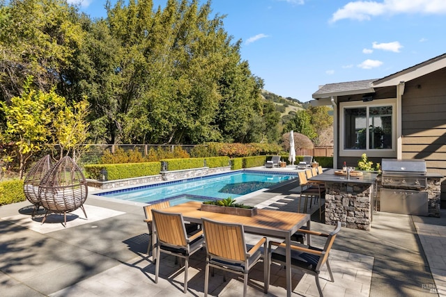 view of swimming pool with a patio, outdoor dining space, fence, a bar, and exterior kitchen