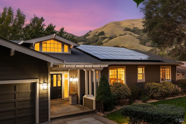 view of front of house with solar panels, a shingled roof, an attached garage, and a mountain view