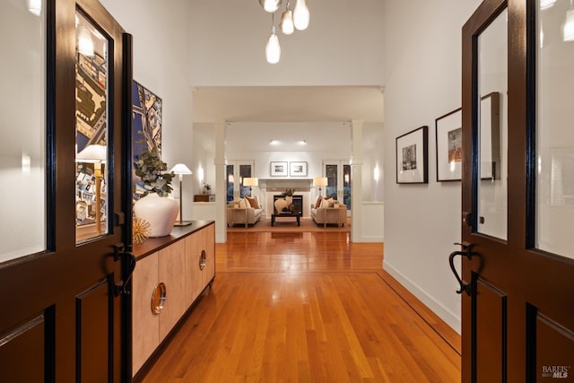 hall featuring light wood-type flooring, baseboards, decorative columns, and a high ceiling