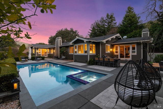 pool at dusk with a pool with connected hot tub, an outdoor bar, and a patio