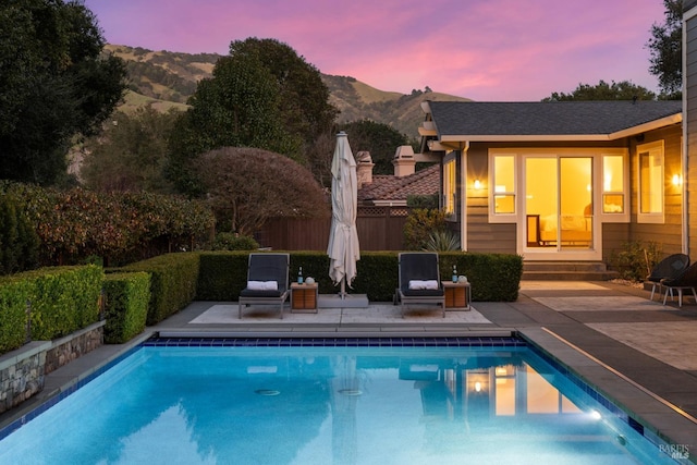 pool at dusk featuring entry steps, a mountain view, fence, a fenced in pool, and a patio area