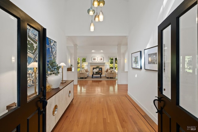 foyer with a fireplace, ornate columns, a towering ceiling, light wood-style floors, and baseboards