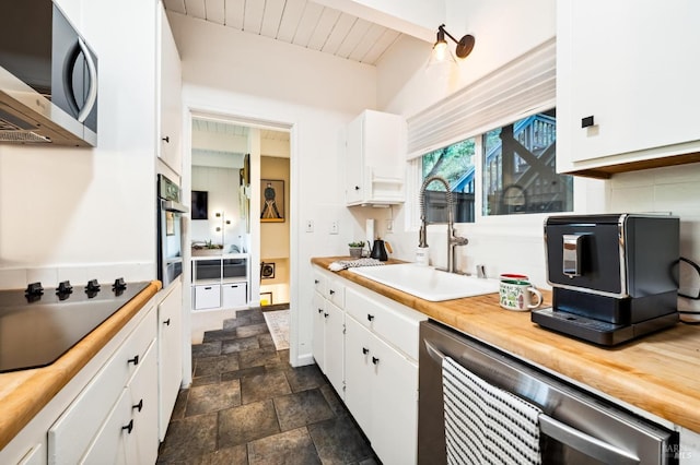 kitchen with butcher block countertops, stainless steel microwave, white cabinets, and a sink