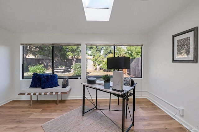 office space featuring vaulted ceiling with skylight, baseboards, and wood finished floors