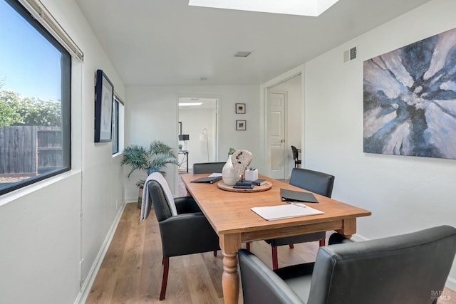 dining room with light wood-type flooring, a skylight, baseboards, and visible vents