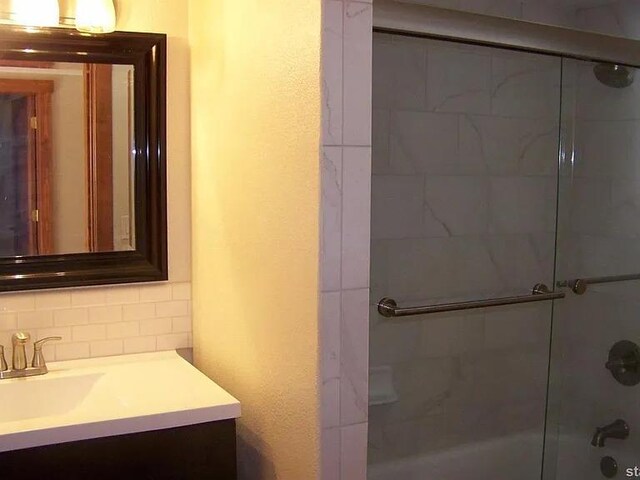 bathroom with bath / shower combo with glass door, tasteful backsplash, and vanity