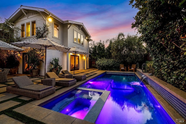 pool at dusk with an outdoor pool, a patio, and an in ground hot tub