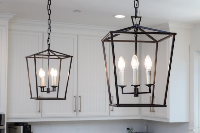 interior details with hanging light fixtures, white cabinets, and crown molding