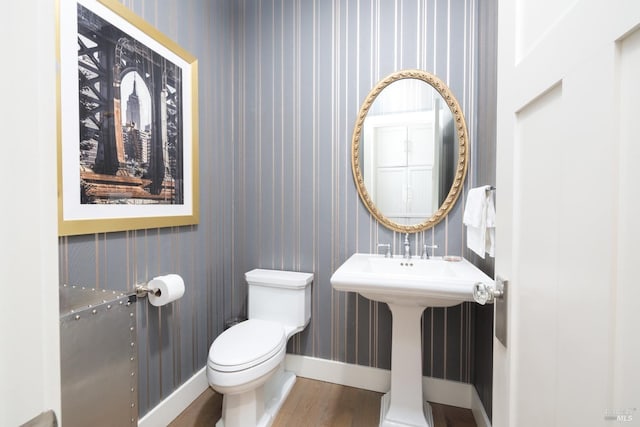 half bath with toilet, wallpapered walls, baseboards, and wood finished floors