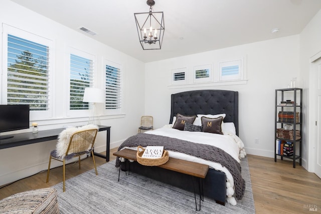 bedroom with visible vents, an inviting chandelier, built in study area, wood finished floors, and baseboards