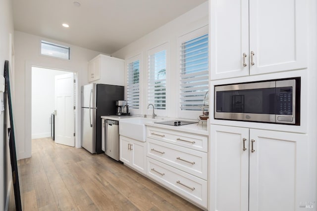 kitchen with appliances with stainless steel finishes, white cabinetry, a sink, and light wood-style flooring