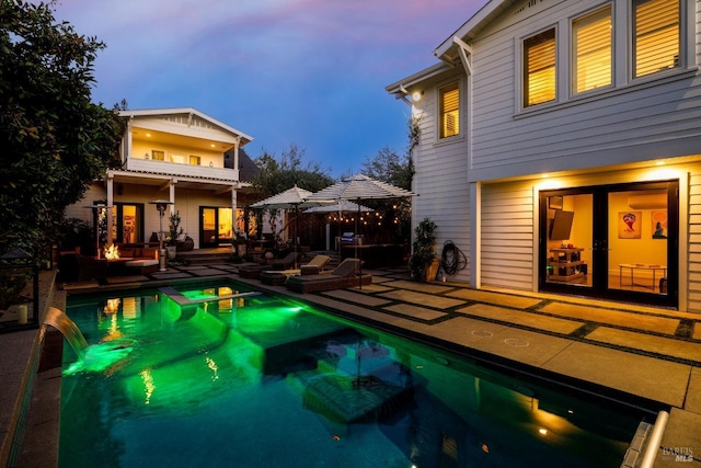 back of house at dusk featuring a patio area, a balcony, and a pool with connected hot tub